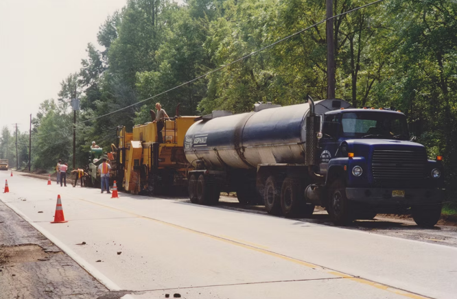 APS crew paving a road with a tanker truck and paving equipment